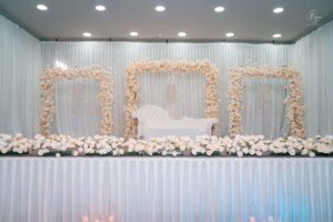 Decorated wedding stage with white settee, curtain backdrop, and floral arches.