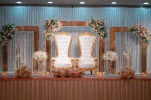 Elaborate wedding stage setup featuring two ornate white and gold throne chairs.