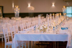 Long wedding dining table set with white tablecloth, candles, and flowers.