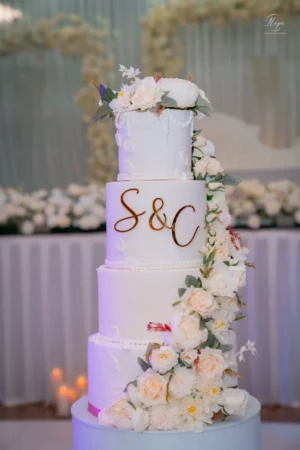 Four-tiered white wedding cake decorated with floral cascading design and monogram.