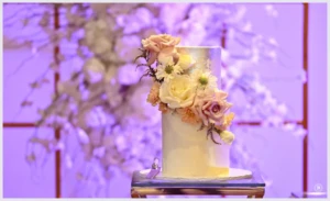 White wedding cake decorated with fresh pastel flowers on a glass stand.