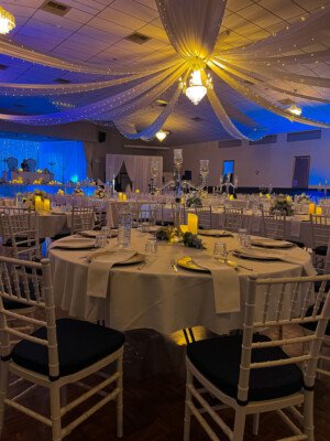 Round banquet table with white tablecloth, tall glass centerpieces, and warm ceiling drapes.