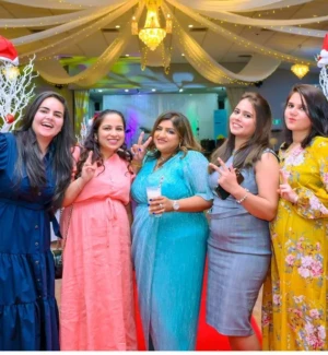 Five women posing happily together in colorful dresses under ceiling drapes.