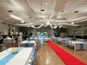 Decorated party hall with blue table runners, a red carpet, and balloon decorations.