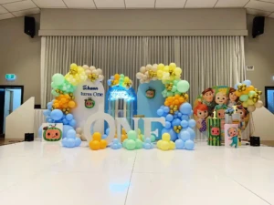 Cocomelon-themed first birthday stage with colorful balloon arches and ONE letters.
