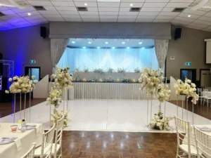 Decorated stage and white dance floor surrounded by white floral stands.