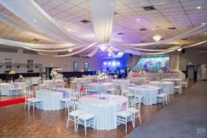Decorated banquet hall with round tables, ceiling drapes, and stage in background.
