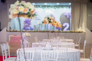 Decorated banquet tables with peach flower centerpieces and a birthday stage in background.