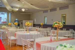 Decorated banquet hall with round tables, peach runners, and tall floral centerpieces.