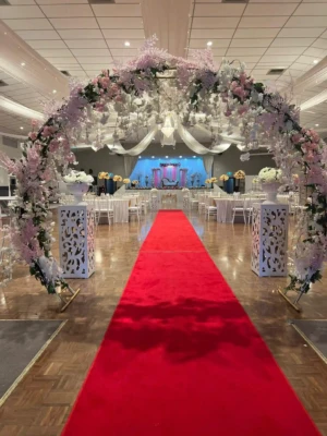 Floral entrance arch leading to a red carpet in a decorated banquet hall.