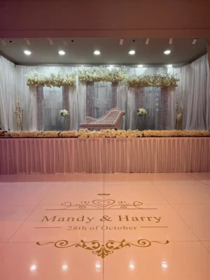 Decorated wedding stage with white couch, white floral backdrop, and personalized floor monogram.