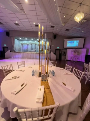 Decorated banquet table with white tablecloth, gold runner, and tall candle centerpiece.