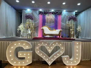 Decorated event stage with white sofa, purple-pink curtains, and illuminated G heart J letters.