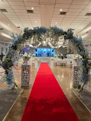 Floral entrance arch leading to a red carpet in a decorated banquet hall.
