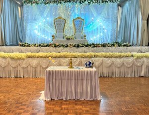 Decorated event stage with gold thrones, white curtains, and glowing ambient lights.